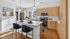 Modern kitchen with sleek white countertops, elegant wood cabinetry, and stainless steel appliances, bathed in natural light.