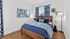 Bright and cozy bedroom showcasing stylish blue decor, elegant wooden furniture, and artistic wall art, bathed in natural light.