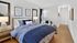 Inviting bedroom with elegant decor, featuring a plush bed with blue bedding, stylish artwork, and soft lighting.