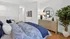 Inviting bedroom with modern decor, featuring a cozy bed with blue accents, stylish dresser, and lush indoor plant.