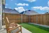 Charming outdoor patio featuring wooden chairs, lush artificial turf, and a privacy fence under a bright blue sky.