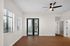 Bright, open living space with sleek wooden flooring and modern ceiling fan, featuring large windows and patio doors with blinds.