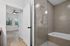 Contemporary bathroom with luxurious tiled shower and inviting bathtub, leading into a bright bedroom with natural light and stylish ceiling fan.