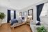 Inviting bedroom with elegant wooden flooring, a plush bed framed by modern art, and natural light filtering through stylish curtains.