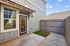 Inviting entrance to a modern home featuring a charming courtyard, sleek gray siding, and stylish window design.