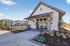 Charming community entrance featuring a modern clubhouse with a sloped roof, surrounded by lush landscaping and welcoming pathways.