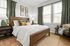 Inviting bedroom with elegant wooden bed, lush green curtains, artistic wall decor, and abundant natural light.