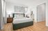 Inviting bedroom with elegant green headboard, light wood floors, and chic framed artwork, leading to a modern ensuite bathroom.