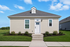 Charming single-story home with light siding, a welcoming front door, and manicured landscaping under a bright blue sky.