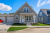 Charming modern home with crisp gray siding, inviting front porch, and beautifully manicured lawn under a bright blue sky.