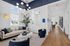 Modern living room with elegant decor, featuring a stylish beige sofa with vibrant cushions, sleek blue chairs, and a sculptural white coffee table. Large windows and tall indoor plants enhance the airy ambiance, complemented by sophisticated lighting fixtures and a warm wooden floor.