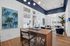 Modern living room with chic decor featuring a stylish wooden desk, contemporary art, plush blue chairs, and abundant natural light.