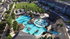 Aerial view of a vibrant apartment community featuring a large, resort-style swimming pool with palm trees and ample lounge seating.