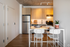 Contemporary apartment kitchen with sleek stainless steel appliances, minimalist cabinetry, and a cozy dining area featuring elegant white chairs and a potted plant.