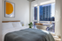 Bright and airy bedroom featuring modern furnishings, a cozy bed, stylish decor, and a large window with a stunning city view.