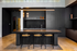Sleek modern kitchen with a black island, wooden chairs, stylish lighting, and elegant cabinetry.
