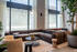 Modern apartment living room with elegant gray sectional sofa, floor-to-ceiling windows, and lush greenery.