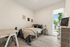 Bright and welcoming bedroom with cozy bed, modern decor, and a sleek desk, bathed in natural light from a large window.