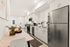 Modern apartment kitchen with sleek stainless steel appliances, elegant white cabinetry, and a cozy dining area adorned with a vase of fresh flowers and a bowl of fruit.