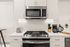 Modern kitchen featuring stainless steel microwave and stove, sleek white cabinetry, and gourmet appliances.