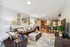 Inviting open-concept living room with a cozy brown leather sofa, chic wall decor, and a modern kitchen with stainless steel appliances in the background.