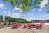 Inviting outdoor patio area with vibrant red picnic tables and chairs around a cozy fire pit, set against a backdrop of lush greenery and modern apartment buildings.