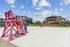 Inviting outdoor area with a sandy volleyball court and vibrant red lifeguard chairs, surrounded by modern apartment buildings.