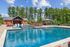 Luxurious swimming pool area with stylish red lounge chairs, brick clubhouse, and a scenic woodland backdrop.