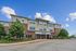 Charming three-story apartment building with modern brick and beige exterior, lush landscaping, and inviting entryway under a clear blue sky.