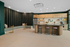 Modern apartment kitchen with sleek wood cabinets, spacious island counter with stylish stools, and elegant green accent walls. Open concept design with cozy seating area and contemporary decor.