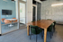 Modern office space featuring a sleek wooden conference table with green chairs, adjacent to a glass-walled meeting room with a round table and soft orange chairs.
