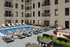 Luxurious apartment courtyard featuring a sparkling pool, sleek sun loungers, and cozy fire pit lounge areas, perfect for relaxation and entertainment.