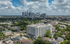 Vibrant urban skyline view featuring a modern mid-rise apartment building, nestled within a lush, green neighborhood under a picturesque cloudy sky.