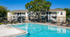 Charming apartment complex with a sparkling swimming pool, ample outdoor seating, and vibrant greenery under a clear blue sky.
