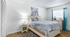 Modern and cozy bedroom with elegant decor, featuring a plush bed with a stylish duvet, soft lighting from a chic lamp, and bright natural light through a window framed with vibrant turquoise curtains.
