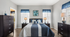 Inviting bedroom with elegant navy and white decor, featuring a plush bed, stylish lamps, and dark wood furniture with natural light flooding through large windows.
