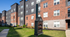 Charming modern apartment building with stylish brick and dark facade, set in a lush green landscape under a clear blue sky.