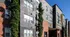 Modern apartment exterior featuring a stylish blend of red and grey brickwork with lush green ivy and large windows.
