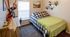 Cozy bedroom with stylish decor featuring a checkered bedspread, vibrant green throw, and a spacious desk under natural light.