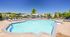 Inviting outdoor swimming pool area with sun loungers and umbrellas under a clear blue sky, surrounded by lush greenery and elegant residential buildings.