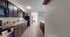 Elegant galley kitchen design featuring dark wood cabinetry, sleek countertops, and modern appliances opening into a bright hallway with a view of a cozy bedroom.