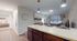 Inviting open-concept apartment showcasing a modern kitchen island with elegant pendant lighting, cozy living area with natural light, and a glimpse into a serene bedroom.