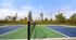 Vibrant outdoor tennis court set against a backdrop of lush green trees and blue sky, ideal for sports enthusiasts.