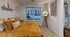 Inviting bedroom with a cozy mustard bedspread, chic decor, and a large window offering a view of modern architecture.