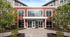 Modern apartment building entrance with large windows and inviting landscaping, featuring a stylish red facade for contemporary urban living.