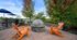 Inviting outdoor patio with modern fire pit, vibrant orange chairs, and lush greenery, perfect for relaxation and gatherings.
