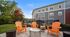 Inviting outdoor space with vibrant orange Adirondack chairs and sleek fire pit, surrounded by lush greenery and modern building backdrop.