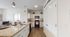 Modern kitchen with sleek white cabinets, cozy dining area, and view into a sunny bedroom.