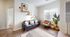 Bright and inviting living room with a modern black sofa, cozy armchair, and stylish decor on floating shelves. Sunlight fills the space through large windows, complemented by wooden flooring and chic houseplants.