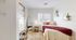 Cozy bedroom with a plush bed adorned with a rich red throw, featuring natural light, elegant mirror, and charming wall art for a welcoming ambiance.
